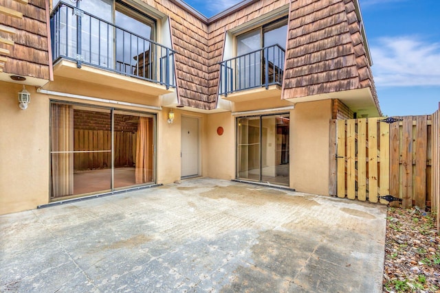 rear view of property with a patio area, stucco siding, fence, and mansard roof