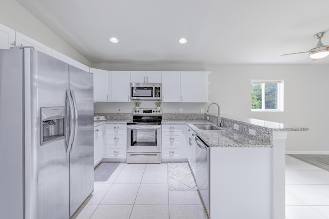 kitchen with white cabinets, appliances with stainless steel finishes, a peninsula, a sink, and light tile patterned flooring