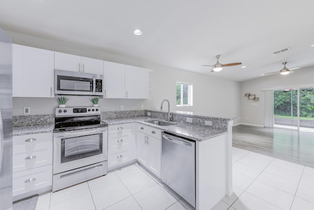 kitchen featuring appliances with stainless steel finishes, open floor plan, white cabinets, a sink, and a peninsula