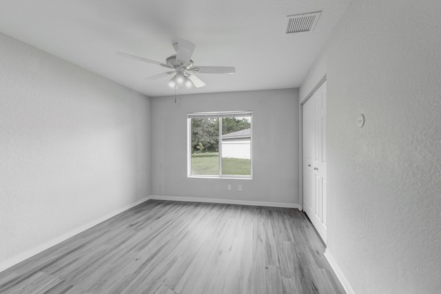 unfurnished room featuring ceiling fan, a textured wall, visible vents, baseboards, and light wood-style floors