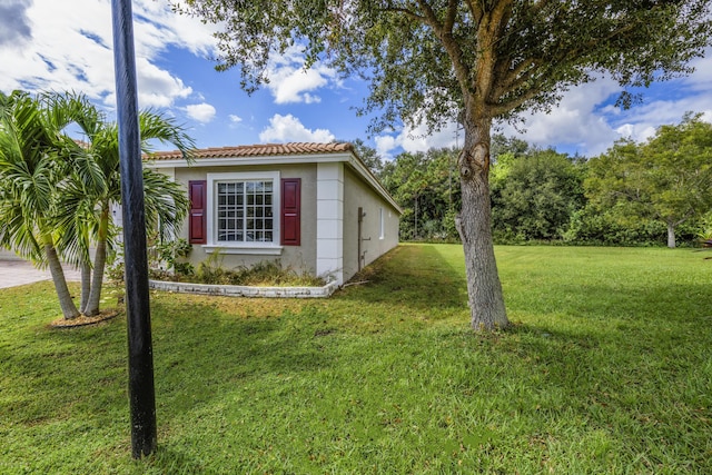 view of side of home featuring a tiled roof, a lawn, and stucco siding