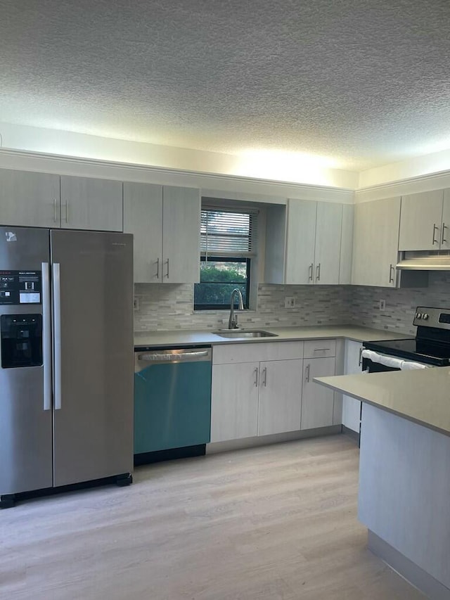 kitchen featuring light countertops, appliances with stainless steel finishes, a sink, and under cabinet range hood