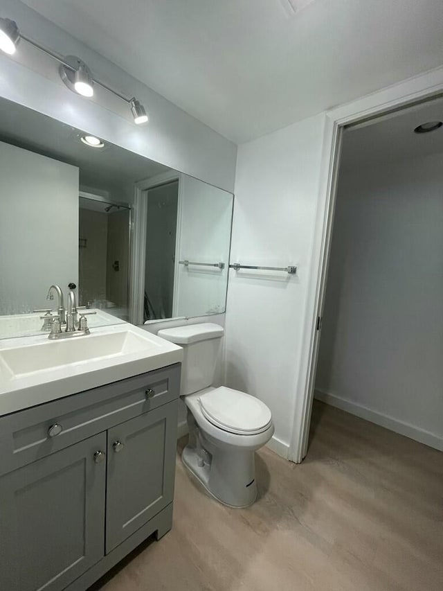 bathroom with toilet, wood finished floors, vanity, baseboards, and walk in shower