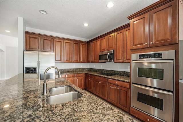 kitchen with dark stone counters, appliances with stainless steel finishes, a sink, and brown cabinets