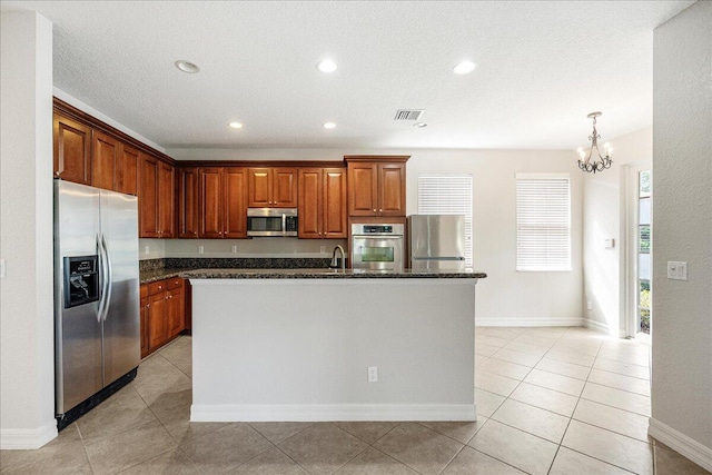 kitchen with decorative light fixtures, a center island with sink, stainless steel appliances, visible vents, and dark stone countertops