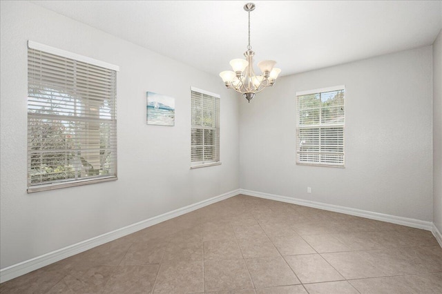 empty room featuring a notable chandelier, baseboards, and light tile patterned floors