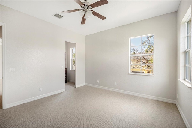 carpeted spare room featuring a wealth of natural light, a ceiling fan, visible vents, and baseboards