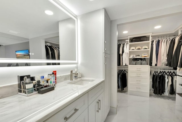 bathroom featuring marble finish floor, a walk in closet, vanity, and recessed lighting