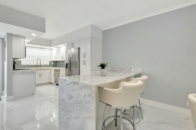 kitchen with light stone counters, a breakfast bar area, stainless steel appliances, white cabinets, and a sink