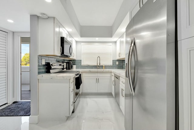 kitchen featuring white cabinets, appliances with stainless steel finishes, a sink, light countertops, and backsplash