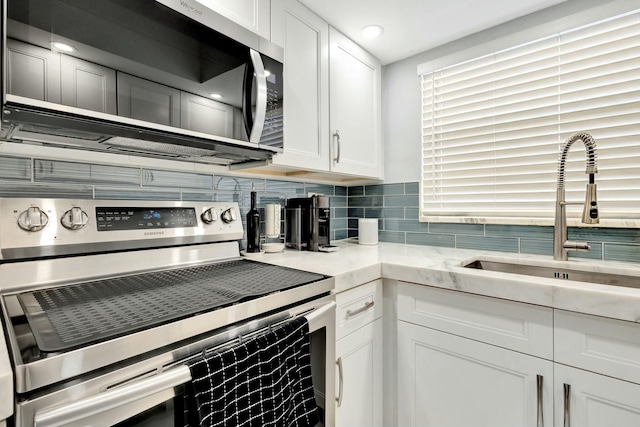 kitchen with light stone counters, a sink, white cabinetry, appliances with stainless steel finishes, and backsplash