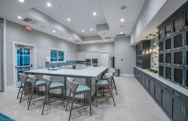 kitchen with visible vents, decorative backsplash, a tray ceiling, a large island with sink, and a sink