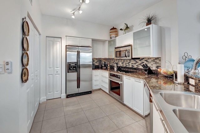 kitchen featuring light tile patterned floors, backsplash, appliances with stainless steel finishes, glass insert cabinets, and a sink