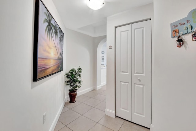 hall with light tile patterned floors, baseboards, and arched walkways