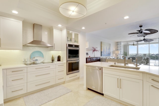 kitchen featuring stainless steel appliances, light countertops, glass insert cabinets, a sink, and wall chimney range hood