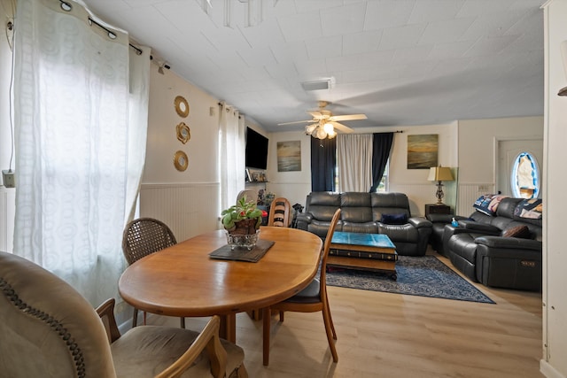 dining space featuring light wood-type flooring, ceiling fan, visible vents, and wainscoting