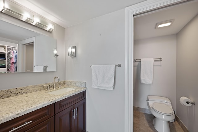 bathroom featuring tile patterned flooring, toilet, vanity, baseboards, and a spacious closet