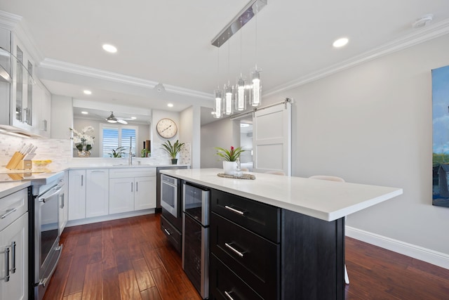 kitchen with a barn door, dark cabinets, white cabinetry, light countertops, and ornamental molding