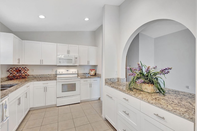 kitchen with white appliances, light stone counters, vaulted ceiling, white cabinetry, and light tile patterned flooring