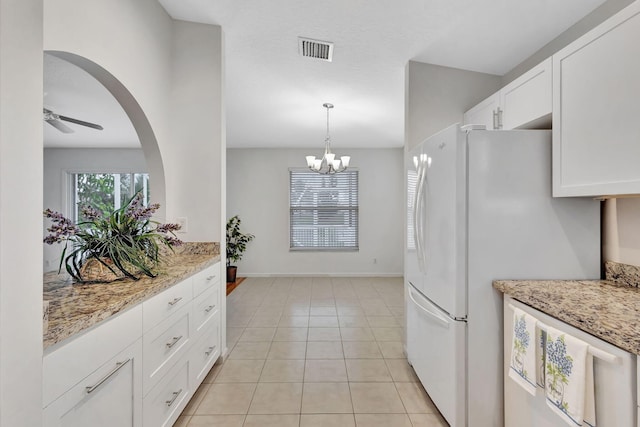 kitchen with visible vents, white cabinets, light stone counters, freestanding refrigerator, and ceiling fan with notable chandelier