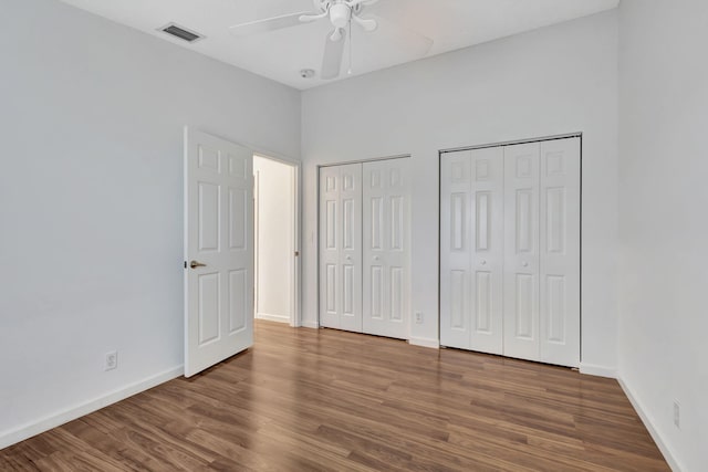 unfurnished bedroom with baseboards, wood finished floors, visible vents, and multiple closets