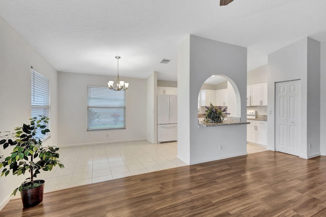 interior space featuring light wood-style floors, visible vents, a textured ceiling, and baseboards