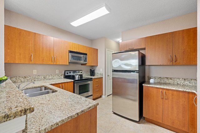 kitchen featuring a peninsula, appliances with stainless steel finishes, brown cabinetry, and a sink