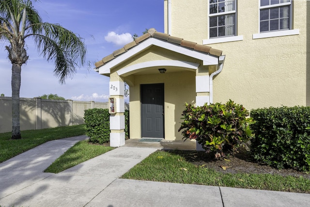 entrance to property featuring fence and stucco siding