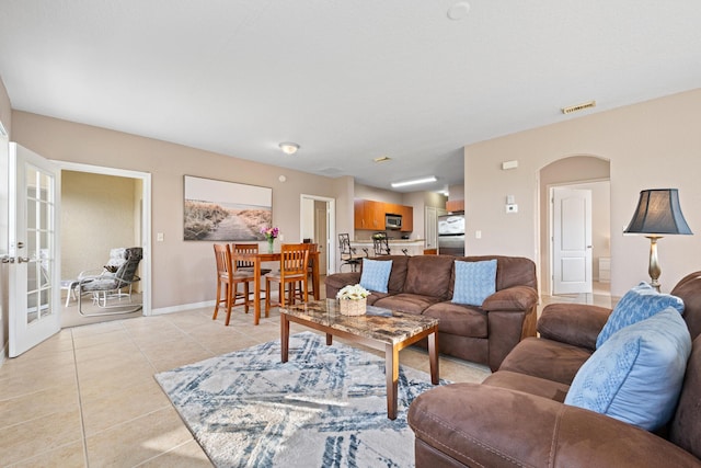 living area featuring light tile patterned floors, baseboards, visible vents, arched walkways, and french doors