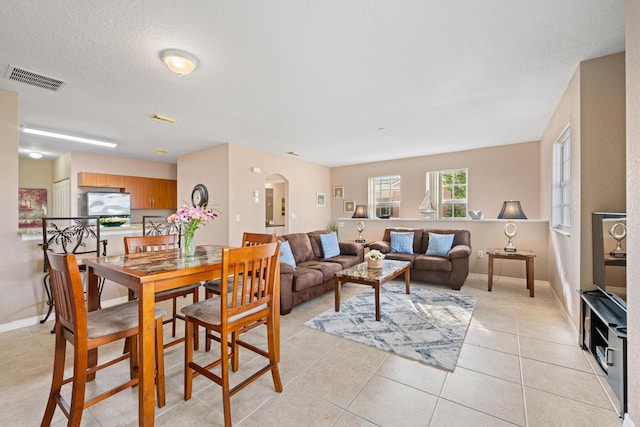 dining space featuring baseboards, visible vents, arched walkways, a textured ceiling, and light tile patterned flooring