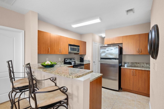 kitchen featuring a peninsula, brown cabinetry, a kitchen bar, and stainless steel appliances