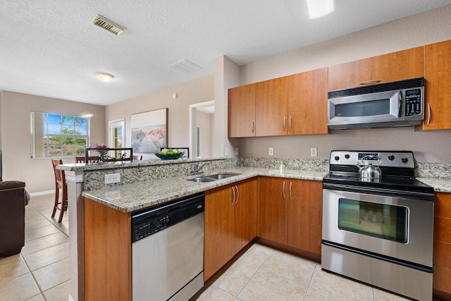 kitchen featuring light stone counters, visible vents, appliances with stainless steel finishes, a sink, and a peninsula