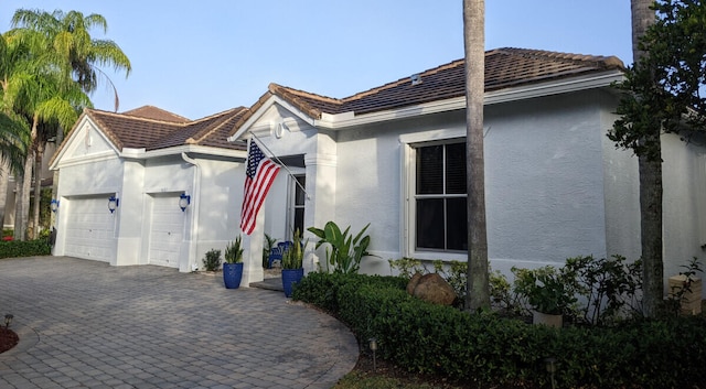 view of front of home featuring a garage, decorative driveway, a tile roof, and stucco siding