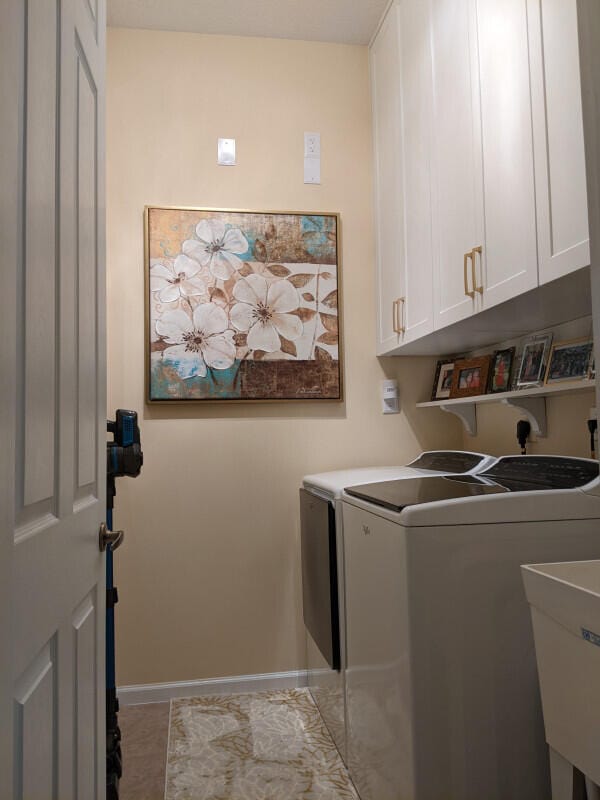 washroom with a sink, washing machine and dryer, cabinet space, and baseboards