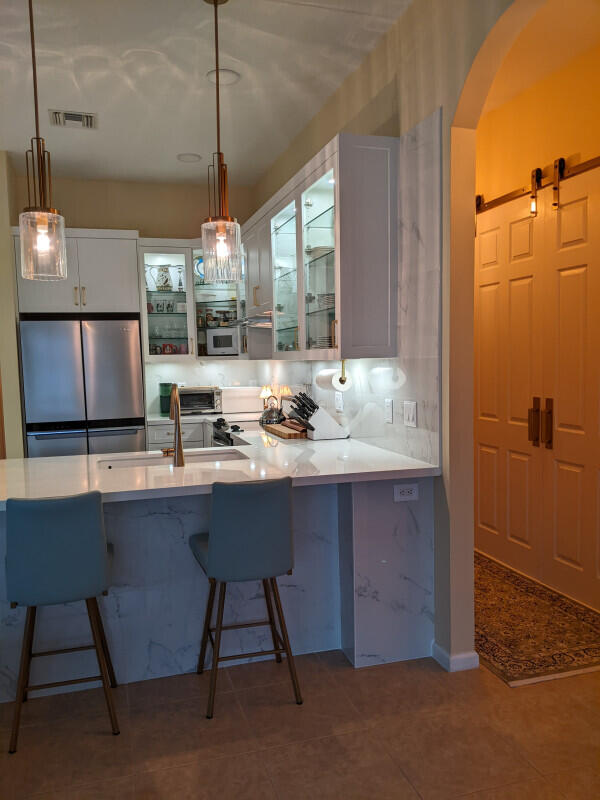 kitchen featuring white cabinets, glass insert cabinets, freestanding refrigerator, hanging light fixtures, and light countertops