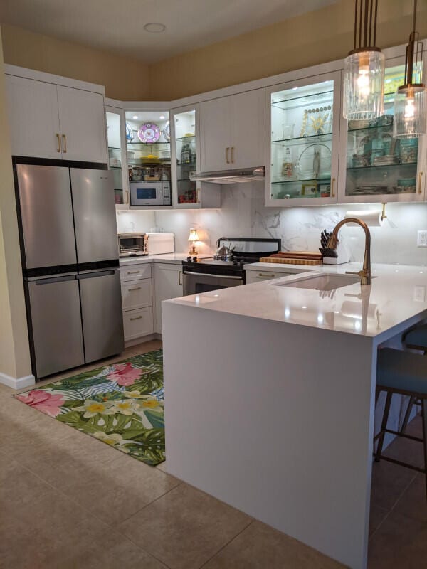 kitchen with pendant lighting, stainless steel appliances, light countertops, white cabinetry, and a sink