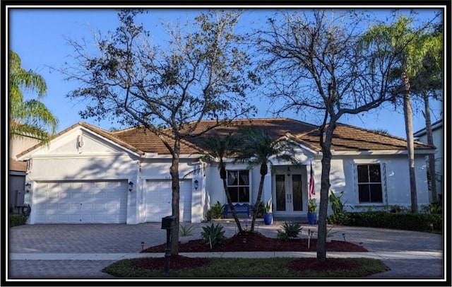 single story home featuring a garage, french doors, decorative driveway, and stucco siding