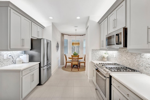 kitchen with light countertops, appliances with stainless steel finishes, hanging light fixtures, and decorative backsplash