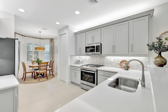 kitchen with stainless steel appliances, light countertops, hanging light fixtures, backsplash, and a sink