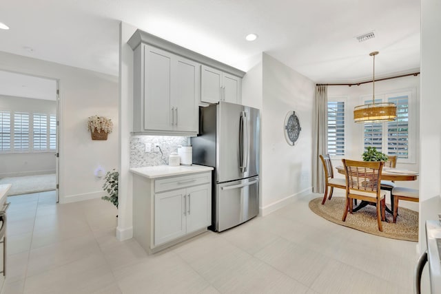 kitchen with light countertops, visible vents, backsplash, freestanding refrigerator, and a healthy amount of sunlight