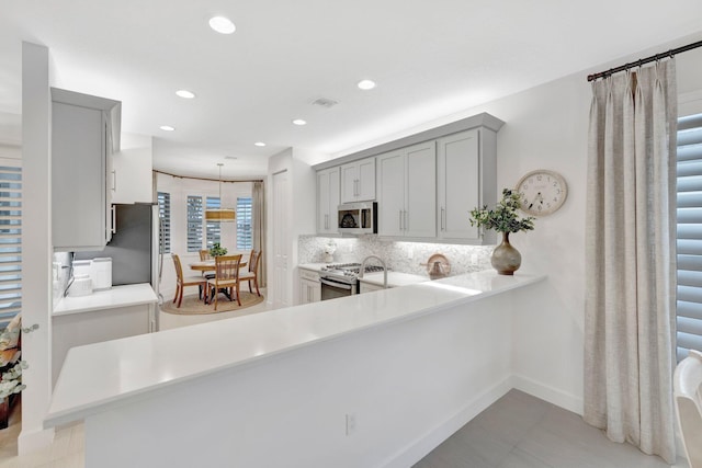 kitchen featuring appliances with stainless steel finishes, decorative light fixtures, a peninsula, gray cabinets, and light countertops