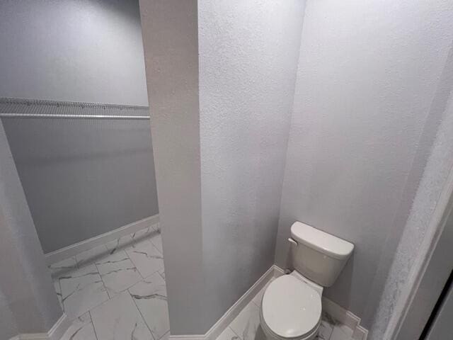 bathroom featuring marble finish floor, toilet, and baseboards