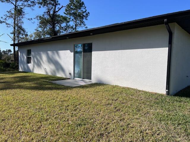 rear view of property featuring a lawn and stucco siding