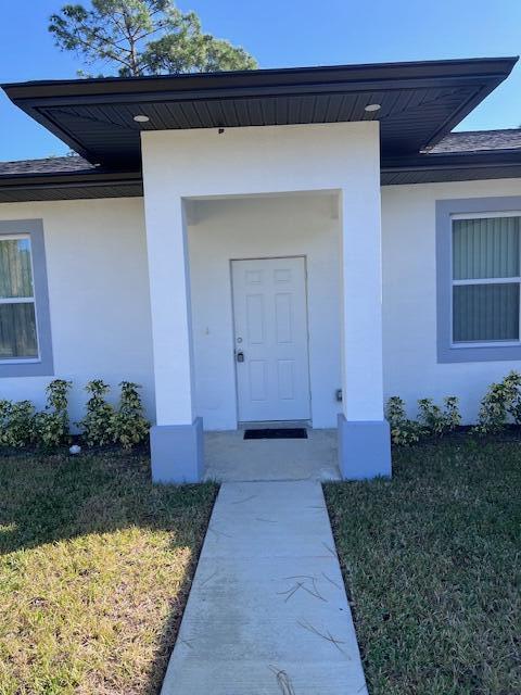 doorway to property featuring a yard and stucco siding