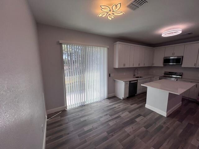 kitchen with stainless steel appliances, light countertops, white cabinets, a kitchen island, and a sink