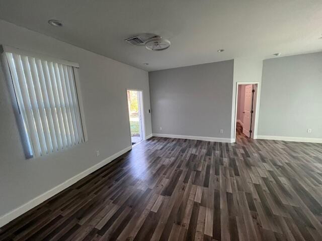 spare room with dark wood-style flooring, visible vents, and baseboards