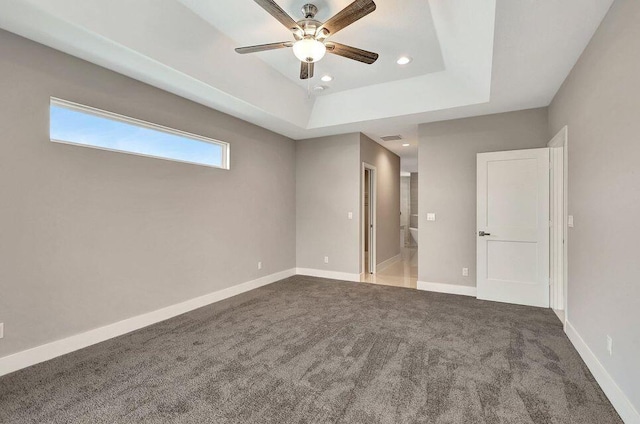 unfurnished bedroom featuring baseboards, ensuite bathroom, a tray ceiling, carpet floors, and recessed lighting