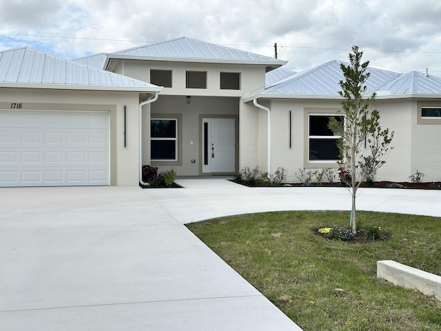 view of front of home with metal roof, a garage, driveway, stucco siding, and a front lawn