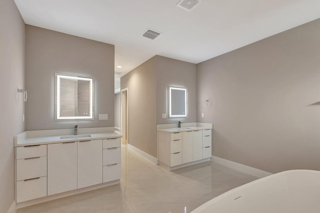 full bath with a freestanding tub, visible vents, two vanities, and a sink