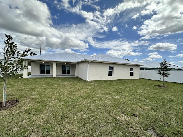 rear view of property featuring metal roof, fence, a lawn, stucco siding, and a patio area